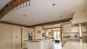 A spacious kitchen with white cabinetry, a central island, and a stone tile floor. - Rose Hips Barn (Chorley)