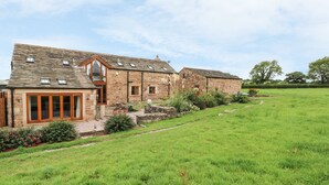 A stone farmhouse with a large glass door entrance, a small patio area, and a well-maintained lawn. - Rose Hips Barn (Chorley)