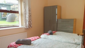 A bedroom with two beds, a wardrobe, and a window with curtains. - West End House (Bradford)