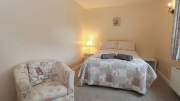 A bedroom with a bed, a nightstand, a lamp, and a floral armchair.