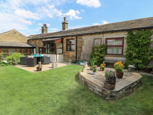 A stone house with a tiled roof, a fenced garden, outdoor furniture, and potted plants.