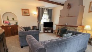 A living room with two grey sofas, a television, a fireplace, and a bookshelf. - West End House (Bradford)