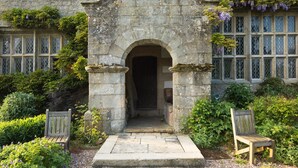 A stone building with a central archway, two wooden benches, and lush greenery. - High Hall (Skipton)