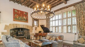 A traditional room with a stone fireplace, a grand piano, and a large window with patterned curtains. - High Hall (Skipton)