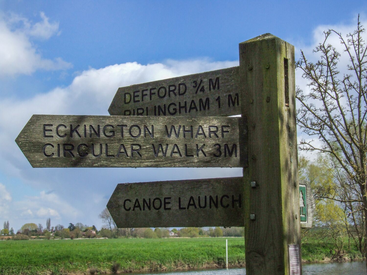 A wooden signpost with directional information for various locations including Deford, Birlingham, Eckington Wharf, Circular Walk, and Canoe Launch.