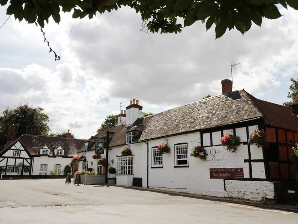 En traditionell vit byggnad med svarta träramar, en skylt med texten ”Queen Elizabeth Inn” och blomkorgar på fönsterbrädorna.