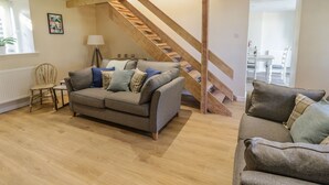 A living room with a wooden staircase, a grey sofa, and a small table with a lamp. - Y Cilgwyn (Blaenau Ffestiniog)