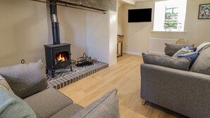 A living room with a stone fireplace, grey sofas, and a television mounted on the wall. - Y Cilgwyn (Blaenau Ffestiniog)