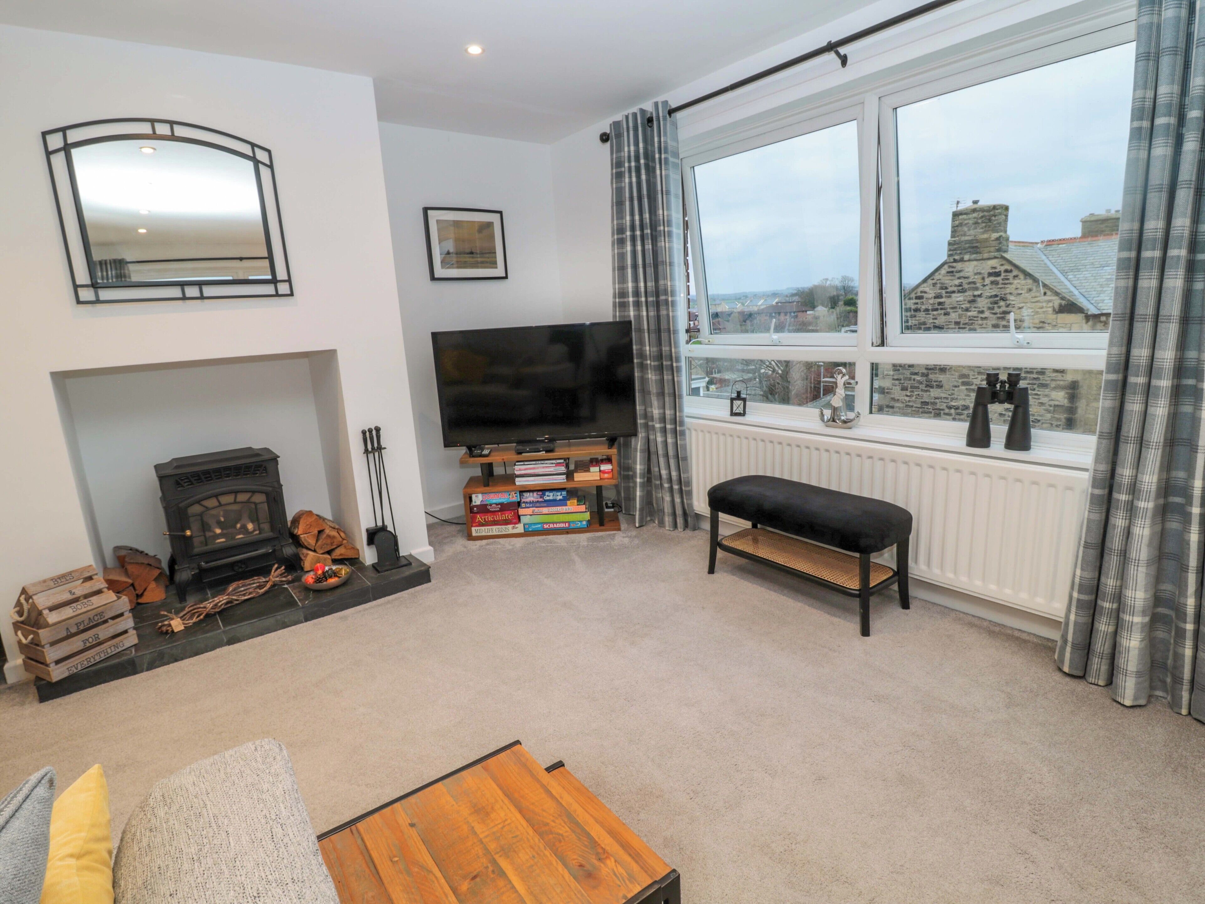A living room with a fireplace, a television, a bench, and a large window with a view of buildings.