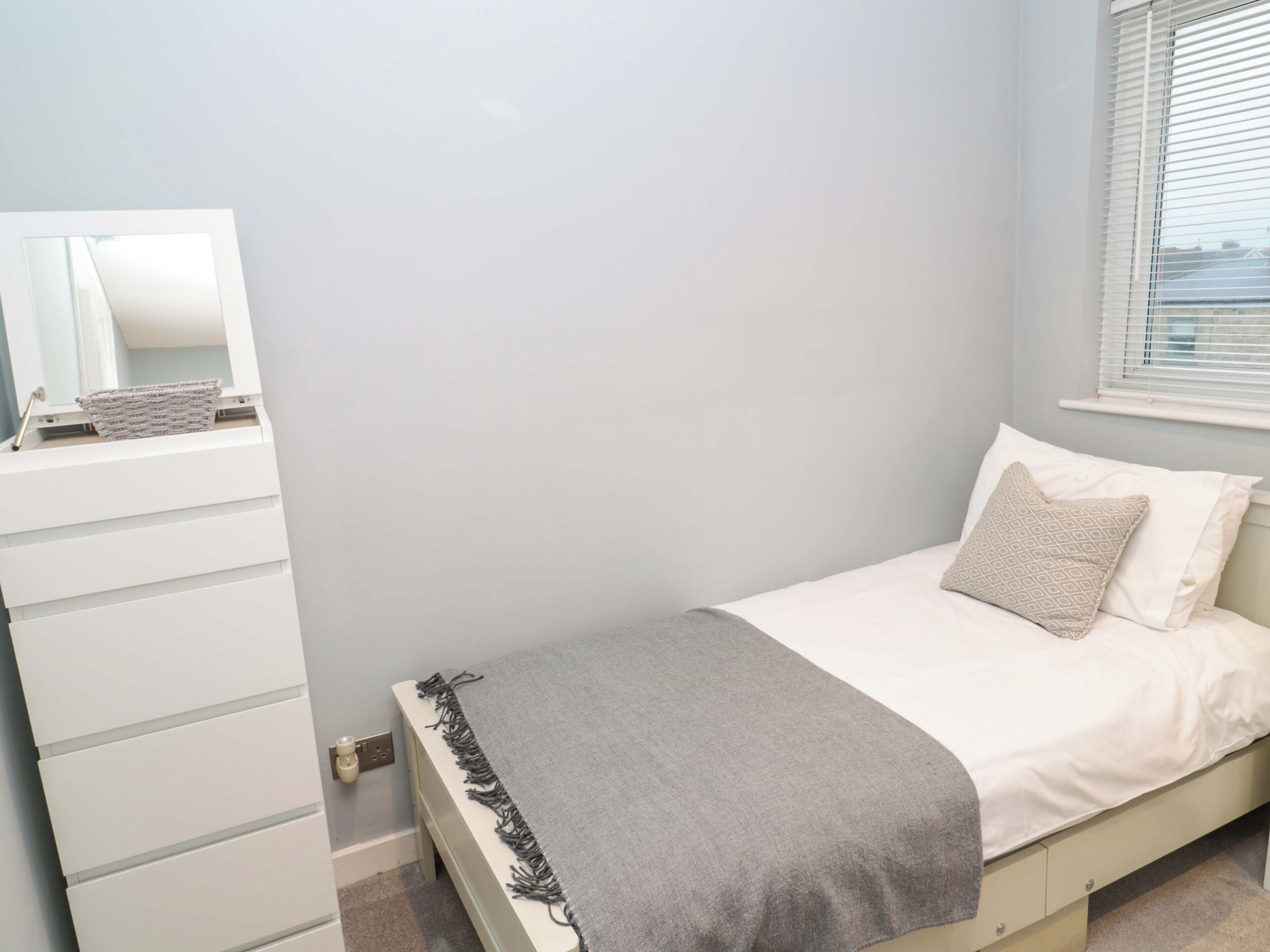 A bedroom with a bed, a dresser, a mirror, and a window with blinds.
