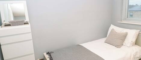 A bedroom with a bed, a dresser, a mirror, and a window with blinds.