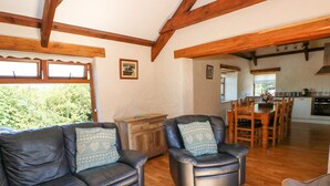 Ein gemütliches Wohnzimmer mit Ledersofa und Sessel, einem Holzesstisch und einer Küche im Hintergrund.