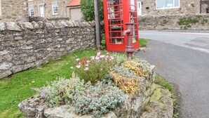 A traditional red telephone booth with a stone wall and flowering plants in front. - Magnolia Cottage (Richmond)