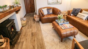 A cozy living room with a fireplace, leather sofas, a coffee table with magazines, and a rug. - Magnolia Cottage (Richmond)