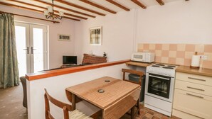 Una cocina compacta con una mesa y sillas de madera, un microondas, un horno y una ventana pequeña.