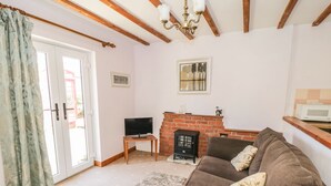 Una sala de estar con un sofá marrón, un televisor sobre una mesa de madera, una chimenea y un ventanal con cortinas.