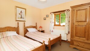A bedroom with two wooden beds, a wardrobe, a window with curtains, and a framed picture on the wall. - Rose Cottage (York)