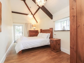 A bedroom with a wooden bed, a nightstand, a dresser, a chandelier, and a window. - Beudy'r Wennol (Caernarfon)