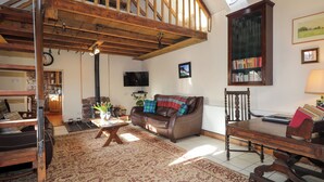 A spacious living room with a high ceiling, a fireplace, a sofa, a coffee table, a bookshelf, and a television. - Milltown House (Turriff)