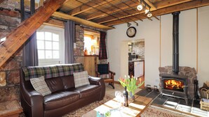 A cozy living room with a brown leather sofa, a wooden coffee table, a stone fireplace, and a rustic staircase. - Milltown House (Turriff)