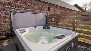 A hot tub in front of a brick building with a wooden fence. - Milltown House (Turriff)