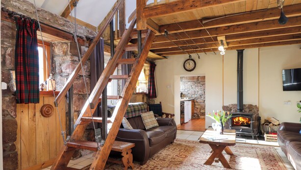 A rustic interior with a wooden staircase, a stone fireplace, and a cozy living area with a sofa and a table. - Milltown House (Turriff)