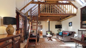 A spacious living room with a high ceiling, wooden beams, a staircase, a fireplace, a television, and a bookshelf. - Milltown House (Turriff)