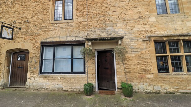 A stone building with a traditional design, featuring a large arched window, a wooden door, and a sign indicating it is a cottage. - The Old Swan (Malmesbury)