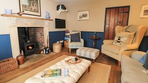 A cozy living room with a fireplace, a comfortable sofa, a cushioned bench, and a small table with a candle. - The Old Swan (Malmesbury)
