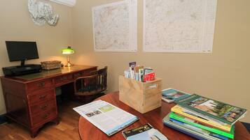 A room with a wooden desk, a computer, a lamp, a chair, a map, and a stack of books.