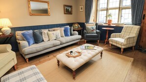A cozy living room with a sofa, armchairs, a coffee table, and a large window with curtains. - The Old Swan (Malmesbury)