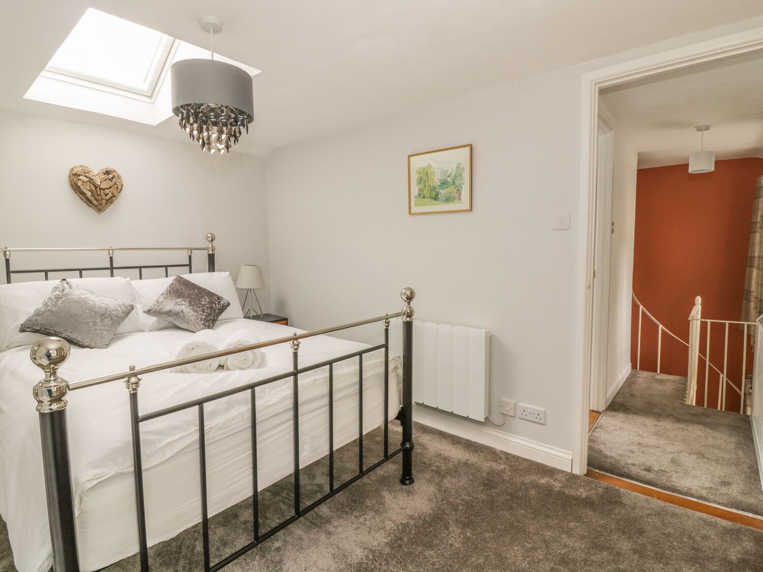 A bedroom with a bed, a radiator, a picture on the wall, and a staircase leading to another room.