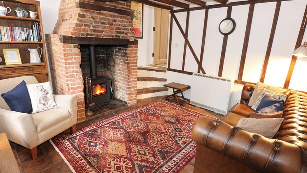 A cozy living room with a brick fireplace, a leather sofa, a patterned rug, and a bookshelf. - Ploughman's (Diss)