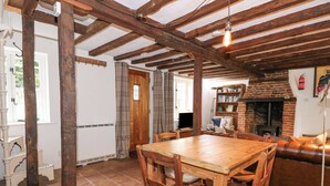 A rustic interior with exposed wooden beams, a brick fireplace, a wooden dining table with chairs, and a leather sofa. - Ploughman's (Diss)