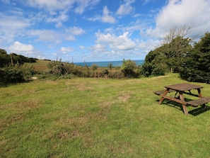 Un campo cubierto de hierba con una mesa de picnic de madera y vista al mar.