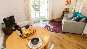 Un comedor con una mesa de madera dispuesta para dos personas, una televisión y un sofá al fondo.