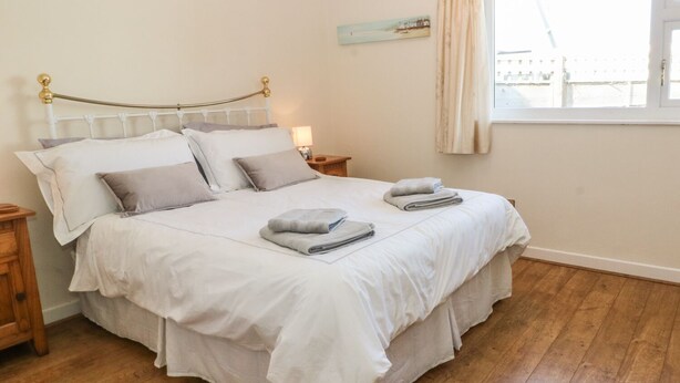 A neatly made bed with white linens, two bedside tables with lamps, a window with curtains, and a painting on the wall. - Trem Y Garn (Pwllheli)