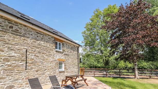 A stone building with a patio area featuring two lounge chairs and a wooden bench.