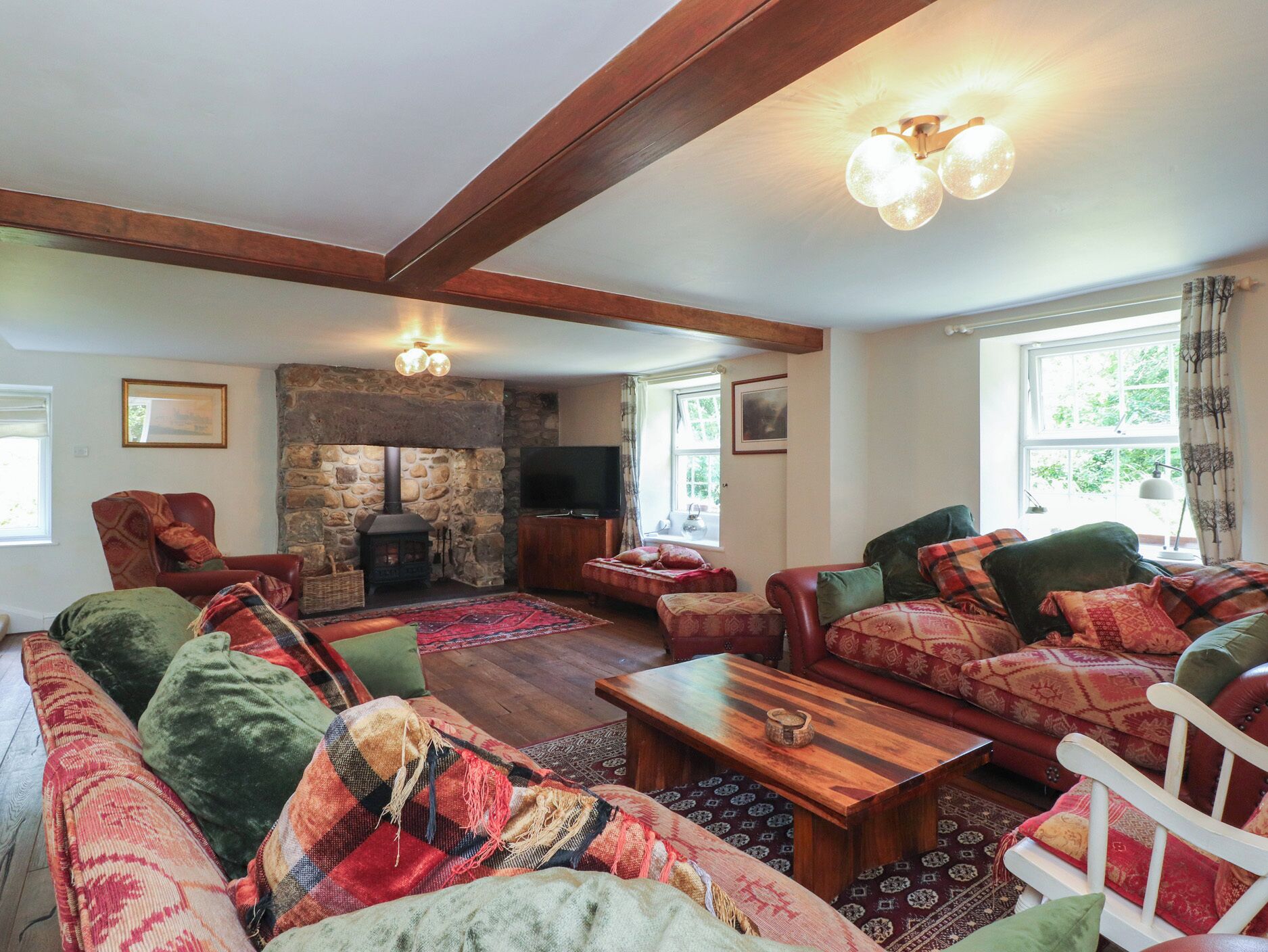 A cozy living room with a stone fireplace, wooden beams, and a large window.