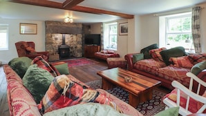 A cozy living room with a stone fireplace, wooden beams, and a large window. - Plas Mawr (Caernarfon)