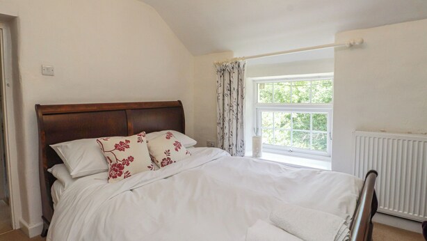A bedroom with a wooden headboard, a large window with curtains, and a radiator. - Plas Mawr (Caernarfon)