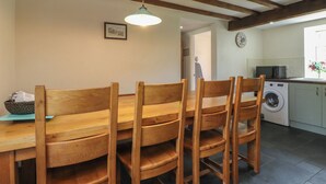A dining area with wooden chairs and a table, a washing machine, and a kitchen area with a clock on the wall. - Plas Mawr (Caernarfon)
