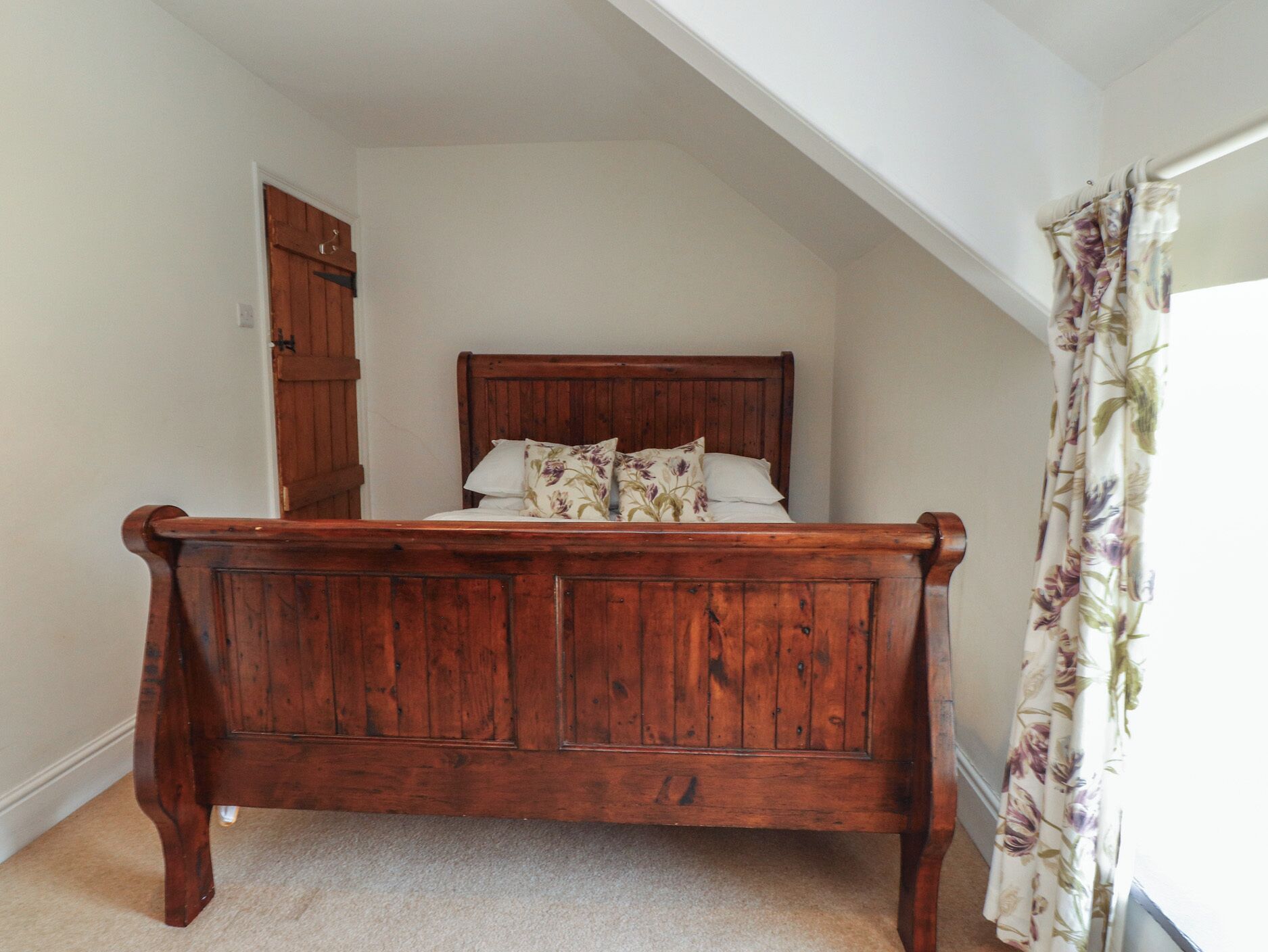 A bedroom with a wooden bed, a door, and a window with floral curtains.