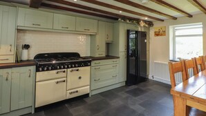 A kitchen with light green cabinets, a black stove, and a black refrigerator. - Plas Mawr (Caernarfon)
