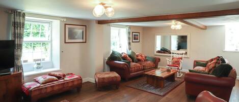 A cozy living room with a sofa set, ottoman, and a television.