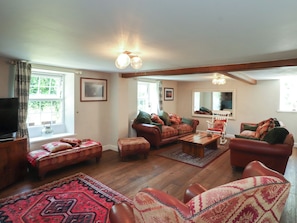 A cozy living room with a sofa set, ottoman, and a television. - Plas Mawr (Caernarfon)