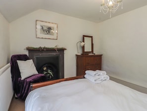 A bedroom with a bed, a chair, a fireplace, a mirror, and a chandelier. - Plas Mawr (Caernarfon)