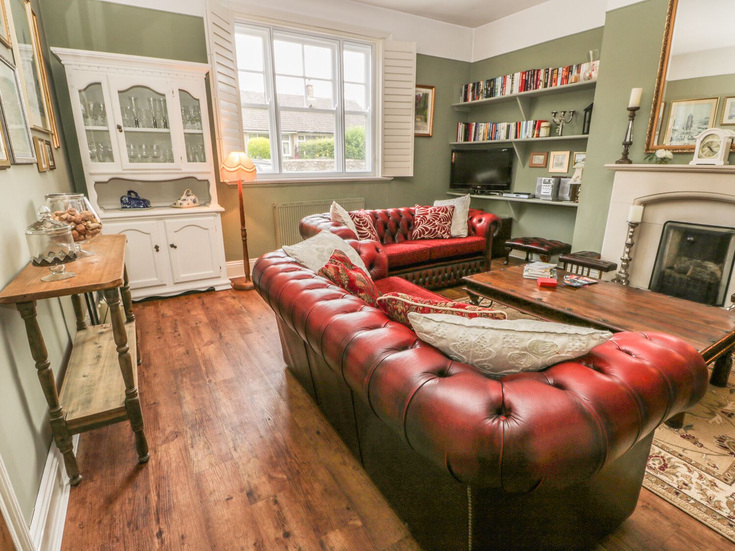 A cozy living room with a red leather sofa, a wooden coffee table, and a bookshelf filled with books.