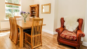 Een eethoek met een houten tafel, stoelen, een boekenkast en een leren fauteuil.