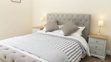 Een netjes opgemaakt bed met een gestuufd hoofdbord, twee nachtkastjes met lampen, en een ingelijste foto aan de muur.